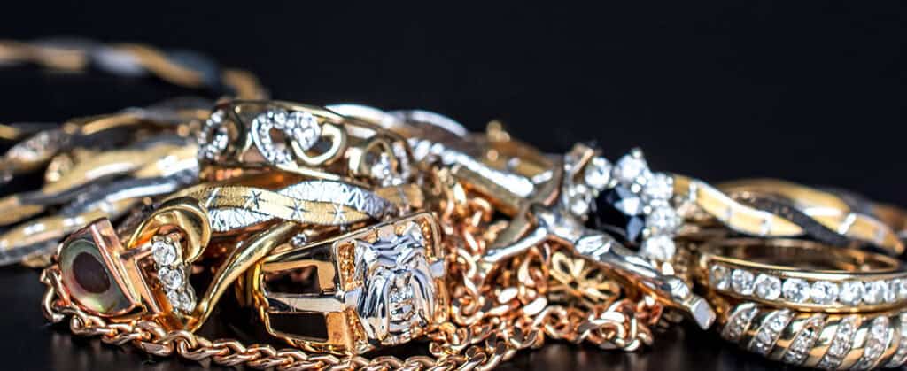 Shiny gold and silver jewelry pieces including rings, necklaces, and bracelets with diamonds and intricate designs, displayed on a black background, showcasing fine craftsmanship and luxury jewelry.