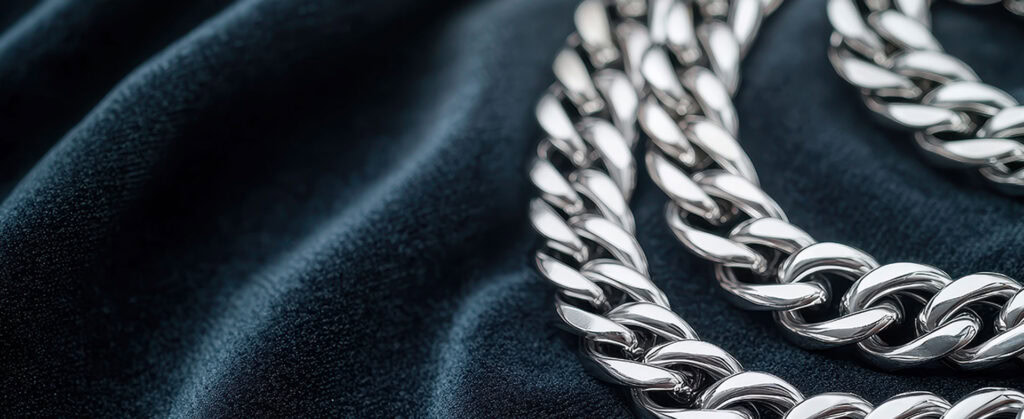 Shiny silver jewelry chain on dark textured fabric, showcasing fine craftsmanship and luxury quality.