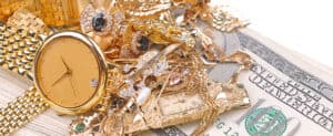 Shiny gold and diamond jewelry including watches, rings, and necklaces piled on cash, showcasing luxury jewelry collections at David Stern Jewelers.
