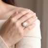 The oval opal halo ring worn on the hand, its white cabochon framed by diamonds in 14kt white gold