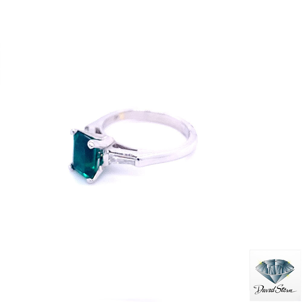 Lab created emerald engagement ring in platinum seen from the left, showing the emerald cut center and baguette side stone