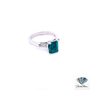 Side view of the emerald cut engagement ring showing the four corner claws and a tapered baguette diamond in the platinum shoulder