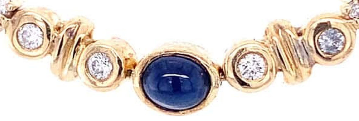 Sapphire station necklace detail: bezel-set oval cabochon sapphire between bezel-set diamonds and grooved gold beads