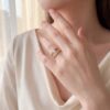 The wide band engagement ring worn on the hand, its 0.70 ct round diamond and channel-set rows in 14kt yellow gold against a cream silk blouse