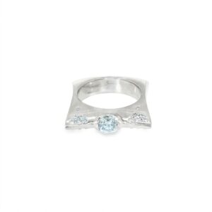 Modern engagement ring seen head on: a low-set round center stone between flush-set diamond clusters on a square brushed 18kt white gold band