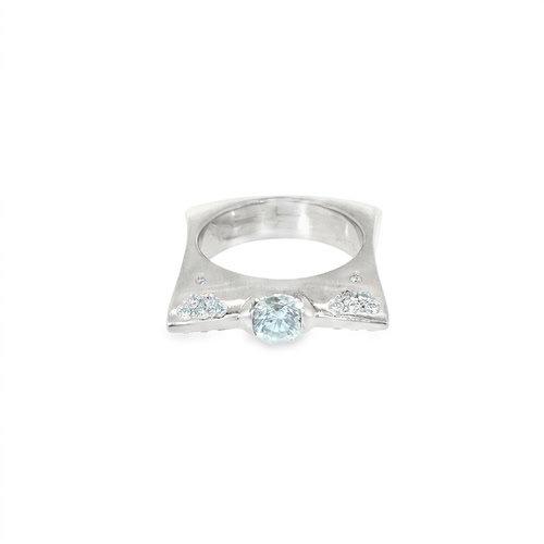 Modern engagement ring seen head on: a low-set round center stone between flush-set diamond clusters on a square brushed 18kt white gold band
