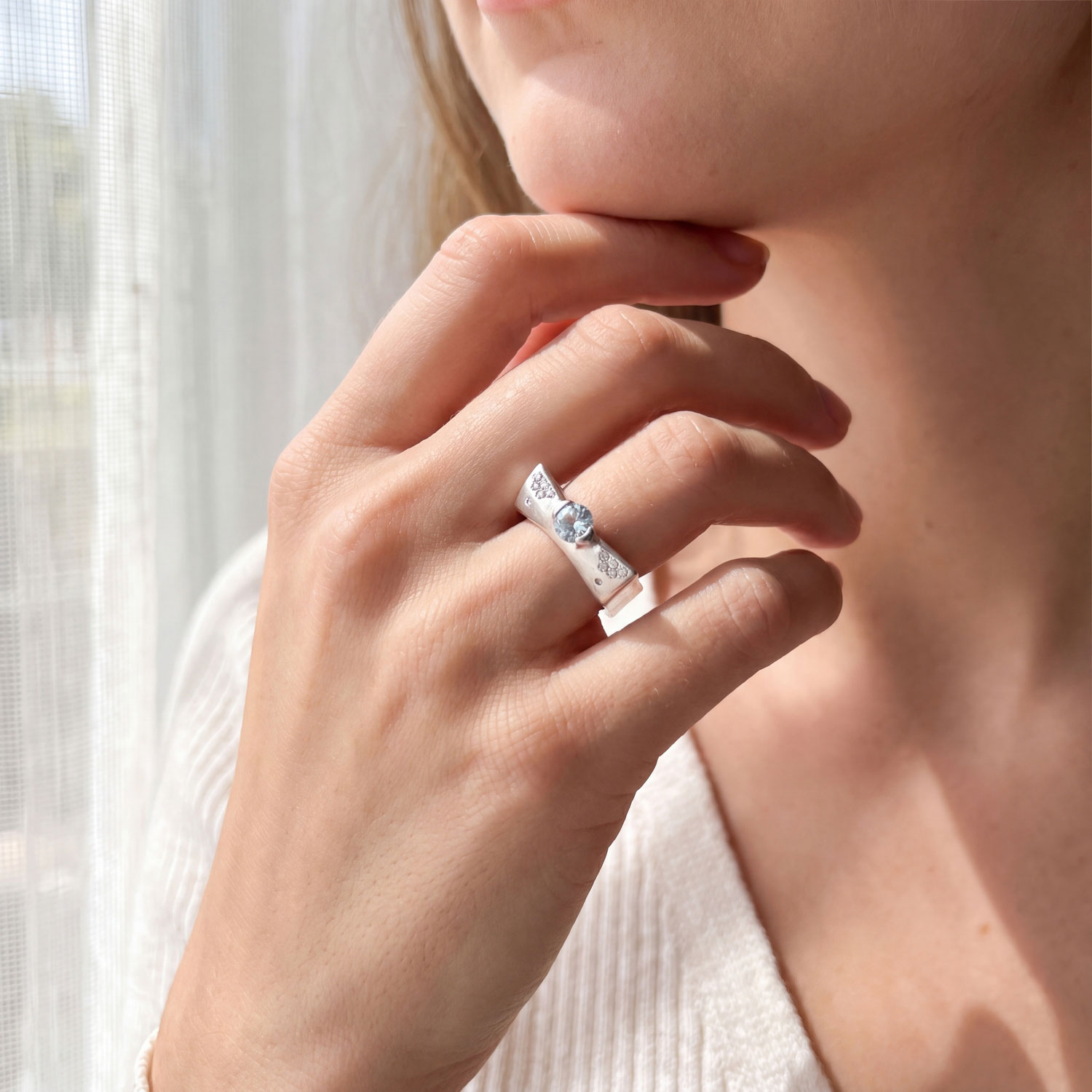 The modern engagement ring worn on the hand, its low-set round center stone between flush-set diamond clusters on a square 18kt white gold band